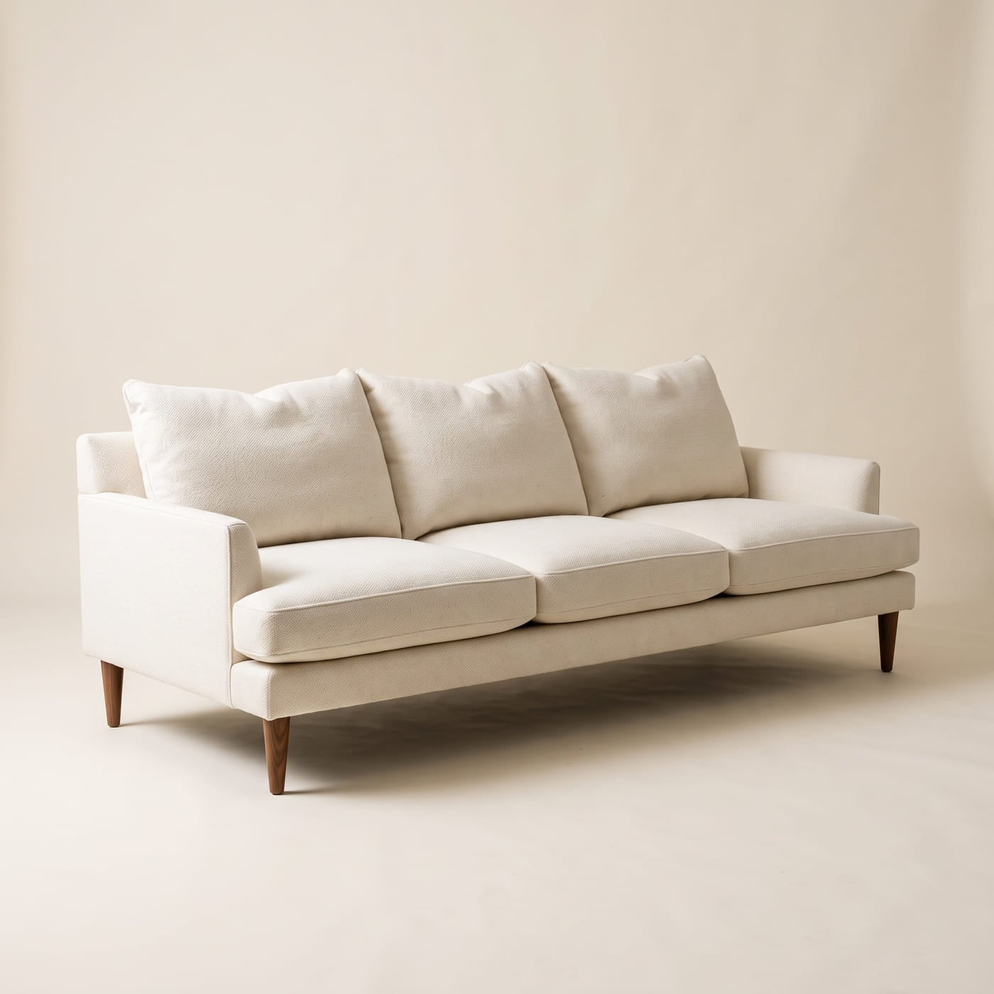 Großes Sofa mit tiefer Sitzfläche in wollweißem Stoff, lose Rückenkissen und schmale Armlehnen auf Holzfüßen.