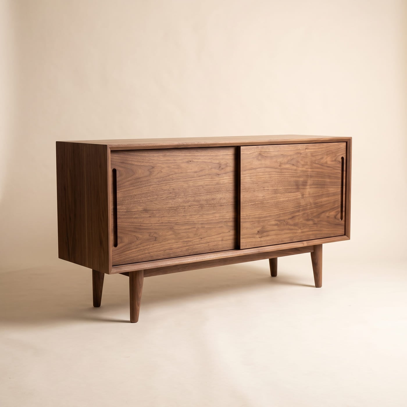 Niedriges Sideboard aus Nussbaum mit zwei Schiebetüren und in die Kante gefrästen Griffmulden.