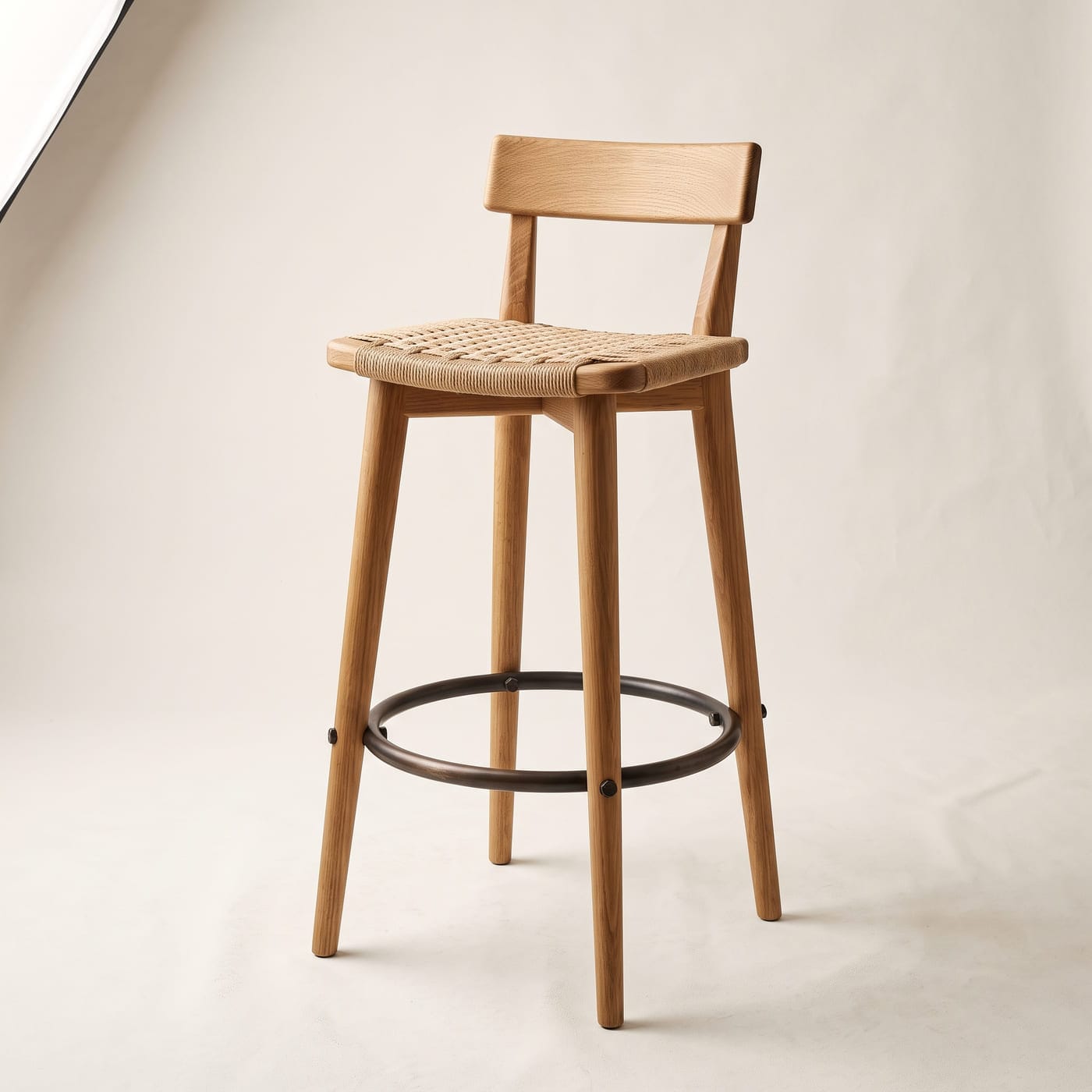 Hoher Holzhocker mit niedriger Rückenlehne und brünierter Fußstütze aus Rundstahl.