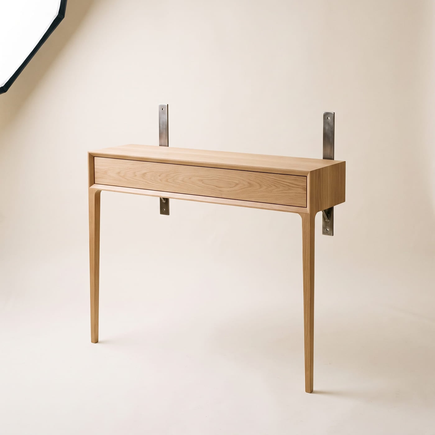 Schmaler Wandtisch mit flacher Schublade über die ganze Breite, auf zwei Beinen und zwei Stahlwinkeln.