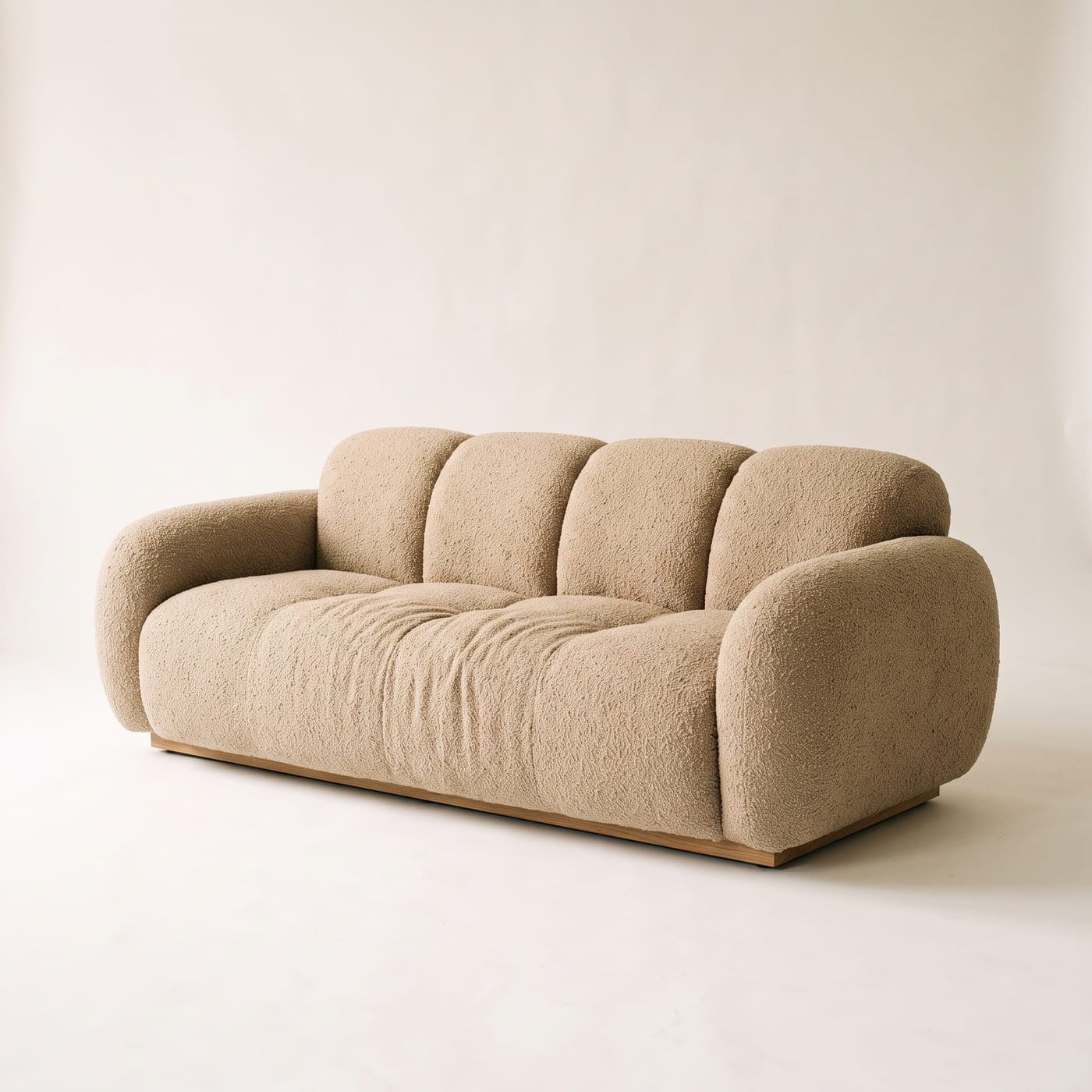 Weiches Sofa mit stark gerundeten Kanten in sandfarbenem Bouclé, tiefe Sitzmulde und volle Rückenkissen.