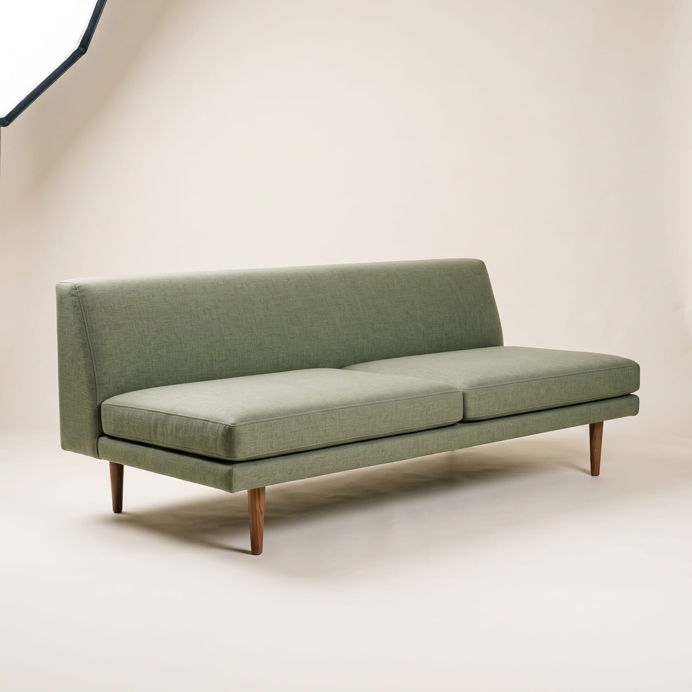 Flaches Sofa mit niedriger fester Rückenlehne in salbeigrünem Leinenstoff auf schlanken Holzfüßen.
