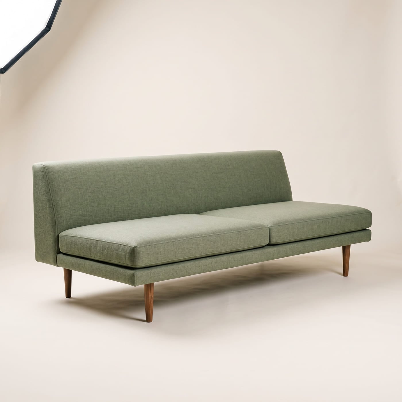 Flaches Sofa mit niedriger fester Rückenlehne in salbeigrünem Leinenstoff auf schlanken Holzfüßen.